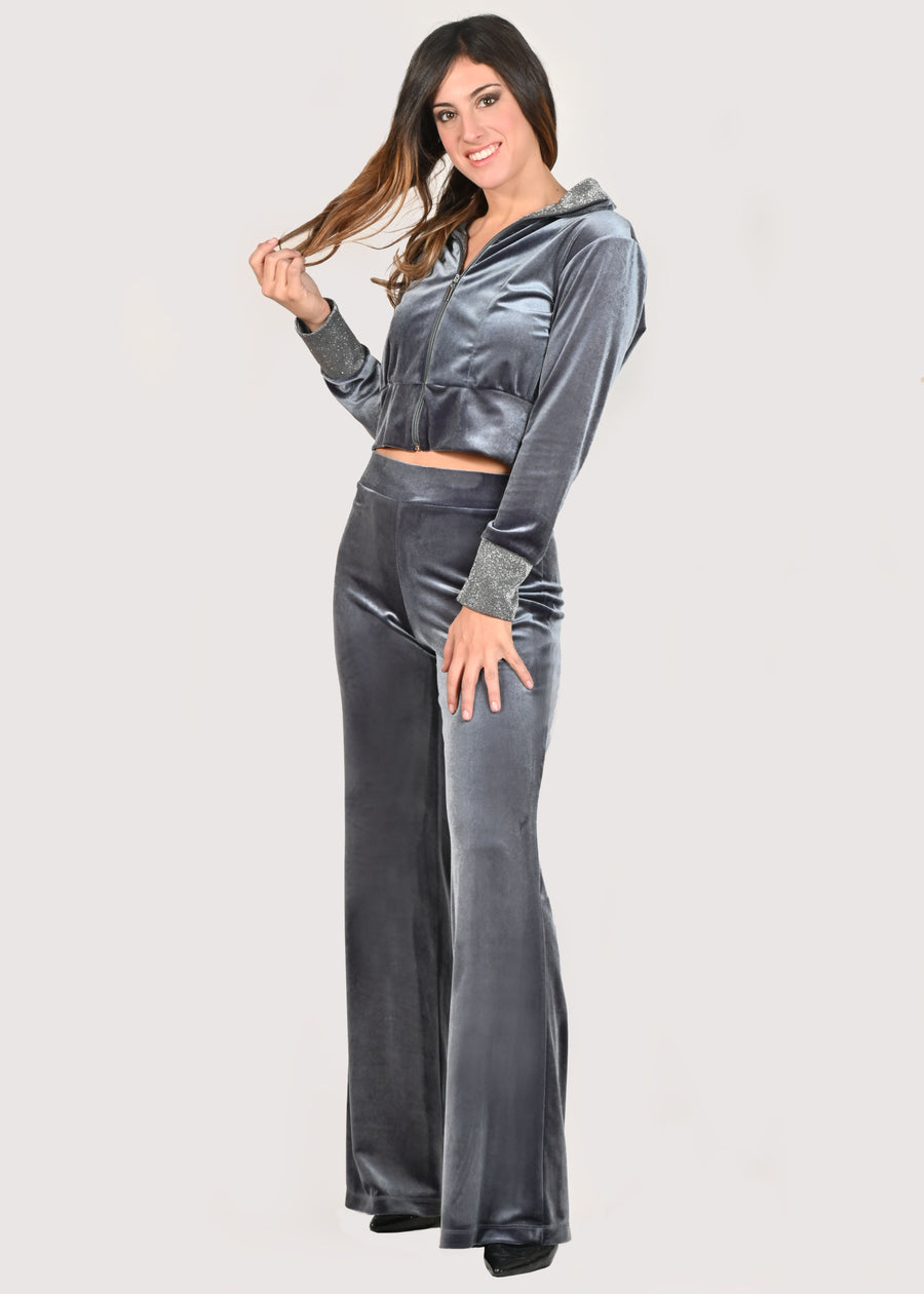 Tuta in velluto elegante grigio perla con taglio crop-top e lurex argento. La tuta senza cappuccio ha il collo ed i polsini in lurex. La felpa crop ha la cerniera lampo nichel free argento, mentre il pantalone palazzo ha la baschina con l'elastico in vita, avvolgendo la silhouette femminile e slanciando la figura. Il tessuto elastico della tuta crop è morbido e confortevole. Le tute in velluto e le tute sportive eleganti sono un'ottima alternativa per sentirsi sempre comode ed trendy. 