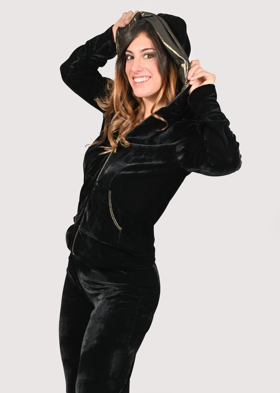 Tuta nera in velluto con inserti in laminato oro. La felpa con cappuccio ha la cerniera lampo nichel free oro, donando eleganza e luminosità all'outfit total black. Il pantalone con elastico in vita è morbido e confortevole. Le tute in velluto e le tute da passeggio eleganti sono un'ottima alternativa per sentirsi sempre comode ed trendy. 