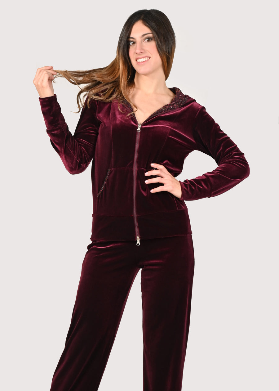 Tuta in velluto elegante bordeaux e lurex. La felpa con cappuccio ha i profili delle tasche in lurex e la cerniera lampo. Il pantalone con elastico in vita è morbido ed elegante. Le tute in velluto e le tute da passeggio eleganti sono un'ottima alternativa per sentirsi sempre comode ed trendy. 