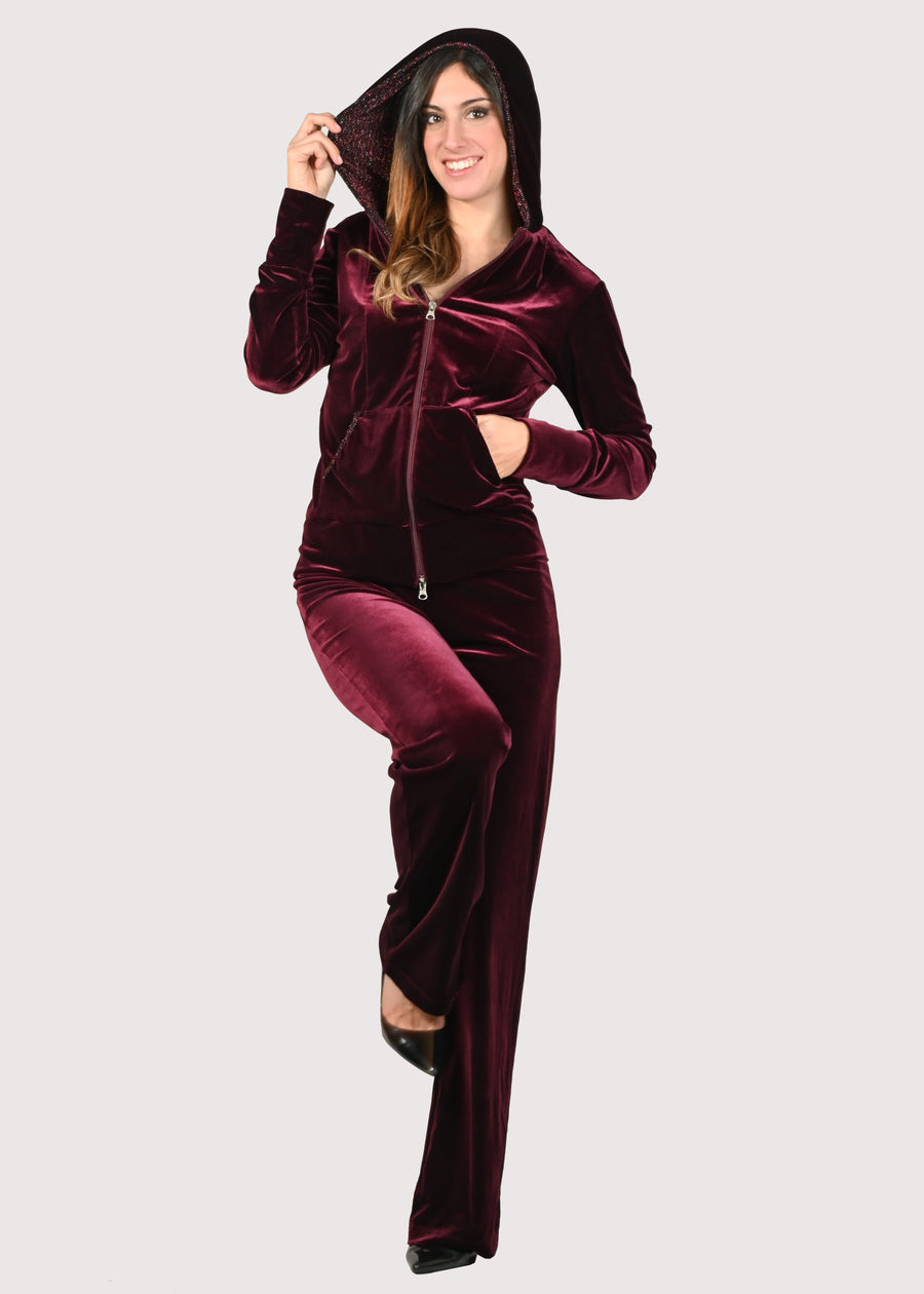 Tuta in velluto elegante bordeaux e lurex. La felpa con cappuccio ha i profili delle tasche in lurex e la cerniera lampo. Il pantalone con elastico in vita è morbido ed elegante. Le tute in velluto e le tute da passeggio eleganti sono un'ottima alternativa per sentirsi sempre comode ed trendy. 