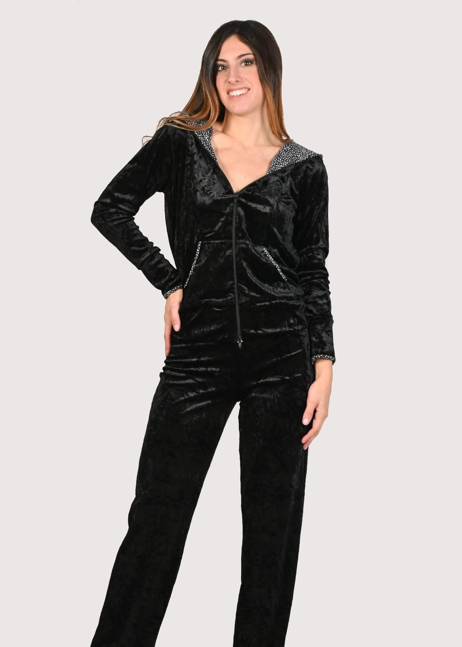 Tuta elegante in velluto nera in velluto martellato. La felpa con capuccio ha la cerniera lampo. Il cappuccio ed i bordi in lurex bronzo/nero donano alla tuta in velluto eleganza e femminilità. Il pantalone con elastico in vita ha la coulisse nell'orlo per poterlo allargare o stringere e avere un effetto remborsè utile anche per evitare di doverlo accorciare. Le tute in velluto e le tute da passeggio eleganti sono un'ottima alternativa per sentirsi sempre comode ed trendy.