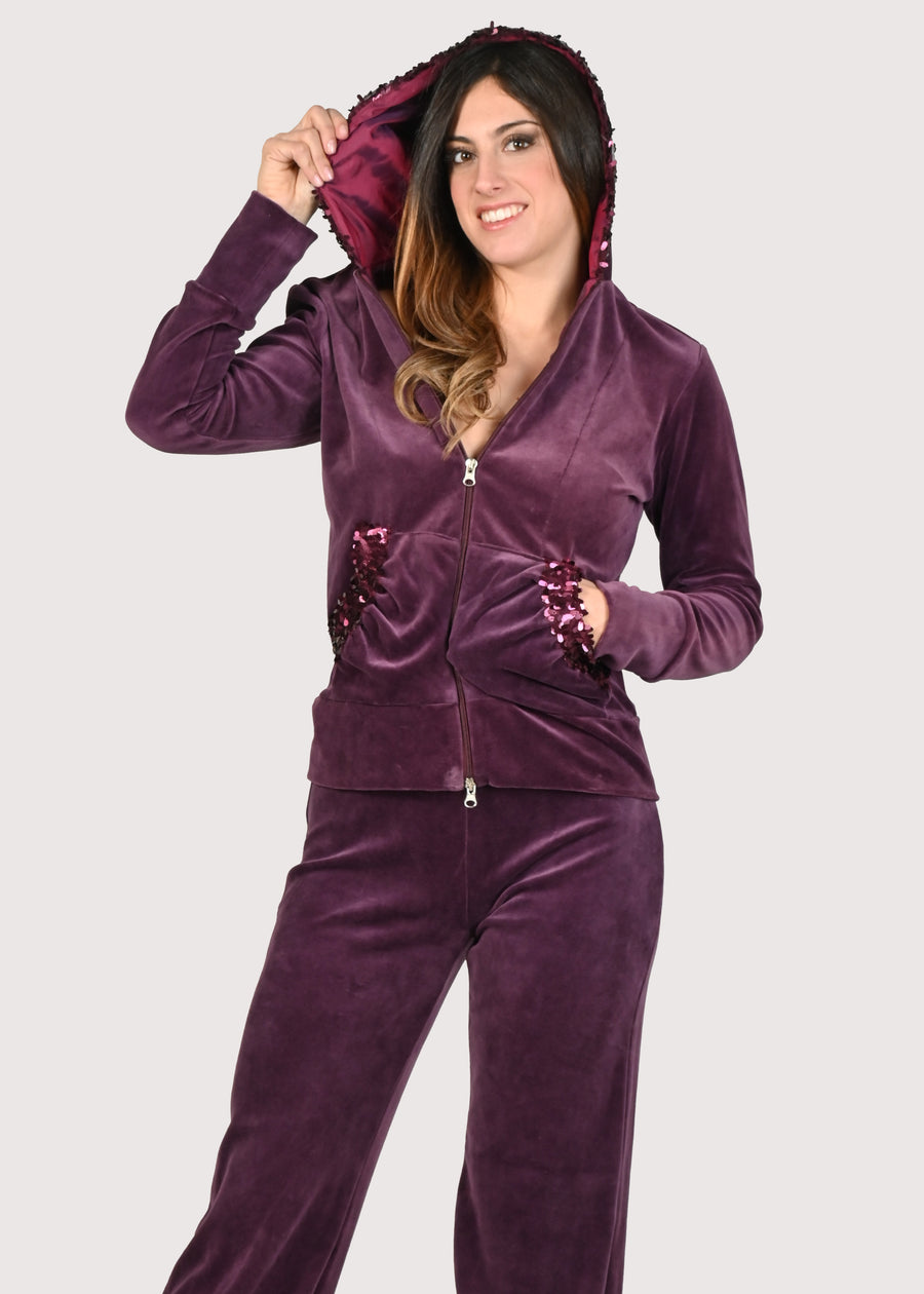 Tuta in ciniglia con paillettes prugna. Tuta elegante tono su tono sulle tasche. La felpa con cappuccio è foderato in taffettas cangiante. Giubbino morbido con cerniera lampo. Il pantalone con elastico in vita ha la coulisse sull'orlo per regolare l'ampiezza e la lunghezza. Le tute in ciniglia e le tute da passeggio eleganti sono un'ottima alternativa per sentirsi sempre comode ed trendy. 