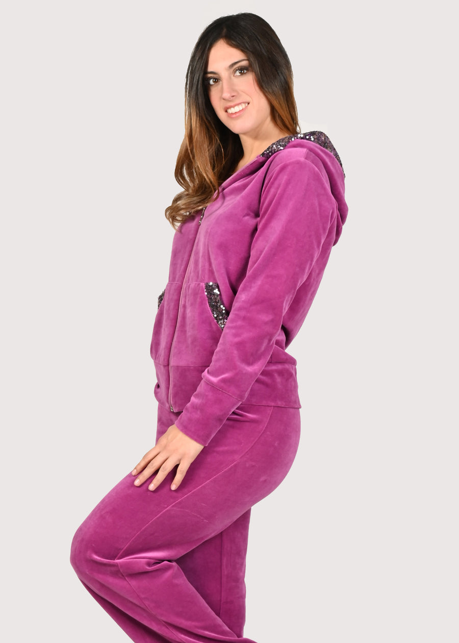 Tuta Completo in ciniglia fucsia sporty chic. La felpa con cappuccio è rifinita internamente e ha gli inserti in paillettes sul cappuccio e sulle tasche. Il pantalone morbido ha un'ottima vestibilità, con l'elastico in vita e la coulisse nell'orlo, per poter regolare la lunghezza del pantalone come si preferisce. Le tute in ciniglia e le tute da passeggio eleganti sono un'ottima alternativa per sentirsi sempre comode ed trendy. 
