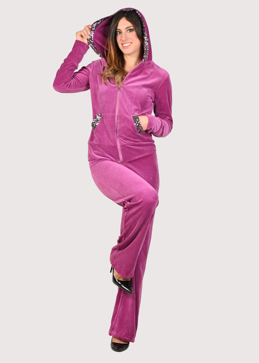 Tuta Completo in ciniglia fucsia sporty chic. La felpa con cappuccio è rifinita internamente e ha gli inserti in paillettes sul cappuccio e sulle tasche. Il pantalone morbido ha un'ottima vestibilità, con l'elastico in vita e la coulisse nell'orlo, per poter regolare la lunghezza del pantalone come si preferisce. Le tute in ciniglia e le tute da passeggio eleganti sono un'ottima alternativa per sentirsi sempre comode ed trendy. 