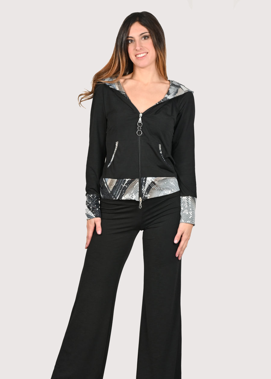 Tuta nera in maglina morbida ed elastica. La jumpsuit ha la cinta, i polsi e l'interno del cappuccio in jersey di paillettes stampata a fantasia. Il pantalone ha la baschina con elastico in vita. L'elasticità del materiale trasferisce comfort al completo elegante.