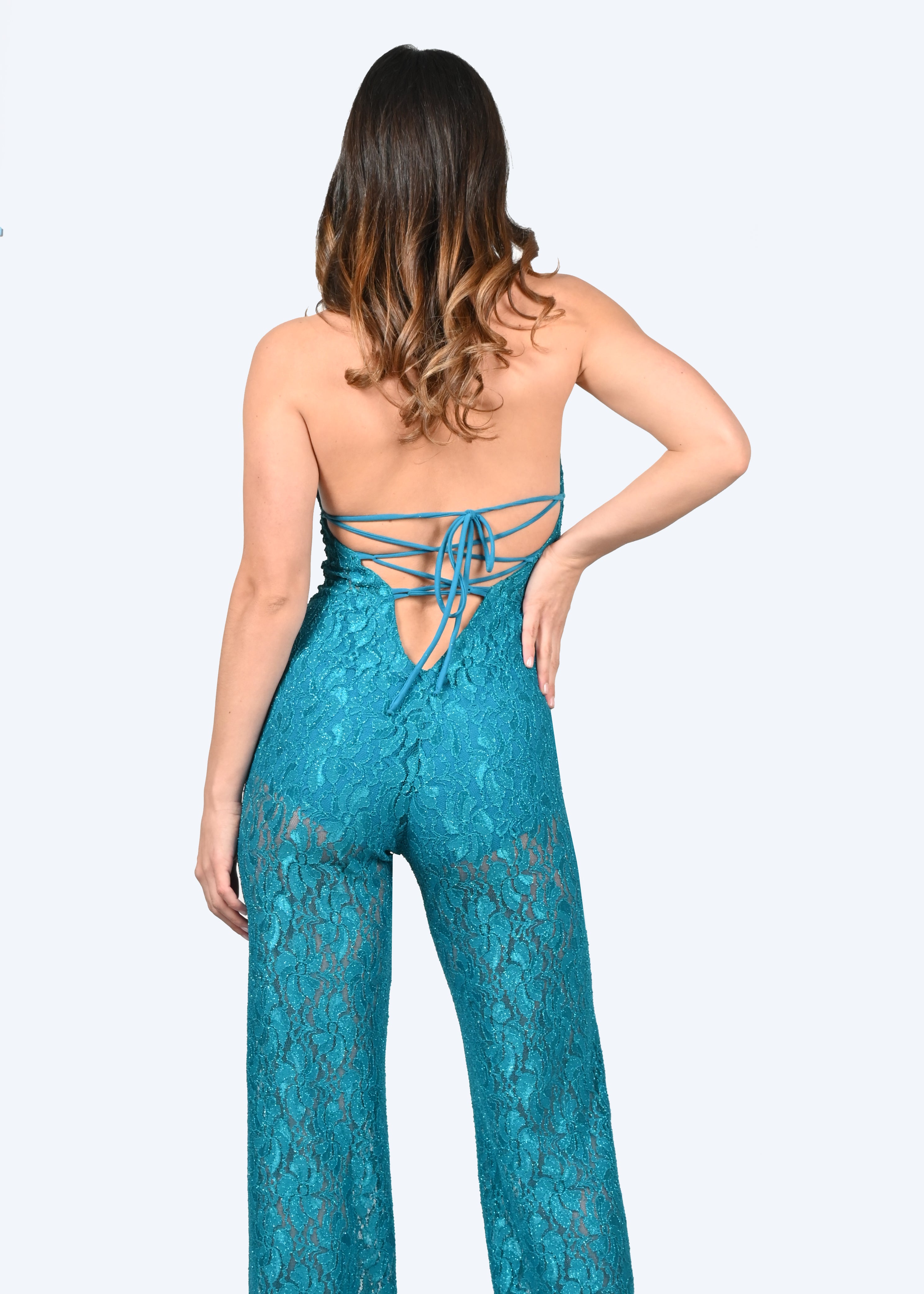 La tuta intera ottanio in pizzo Iris è caratterizzata da un profondo scollo a V lungo la schiena con cappiole e budellini incrociati regolabili. Il pizzo della jumpsuit elegante è impreziosito da un delicato effetto lurex, creando un sensuale effetto vedo non vedo. La tuta intera in pizzo ha la chiusura con bottone ricoperto dietro al collo, coppe estraibili ed è foderata internamente, lasciando l'addome scoperto. Il modello è a vita alta con pantalone dalla linea scivolata.