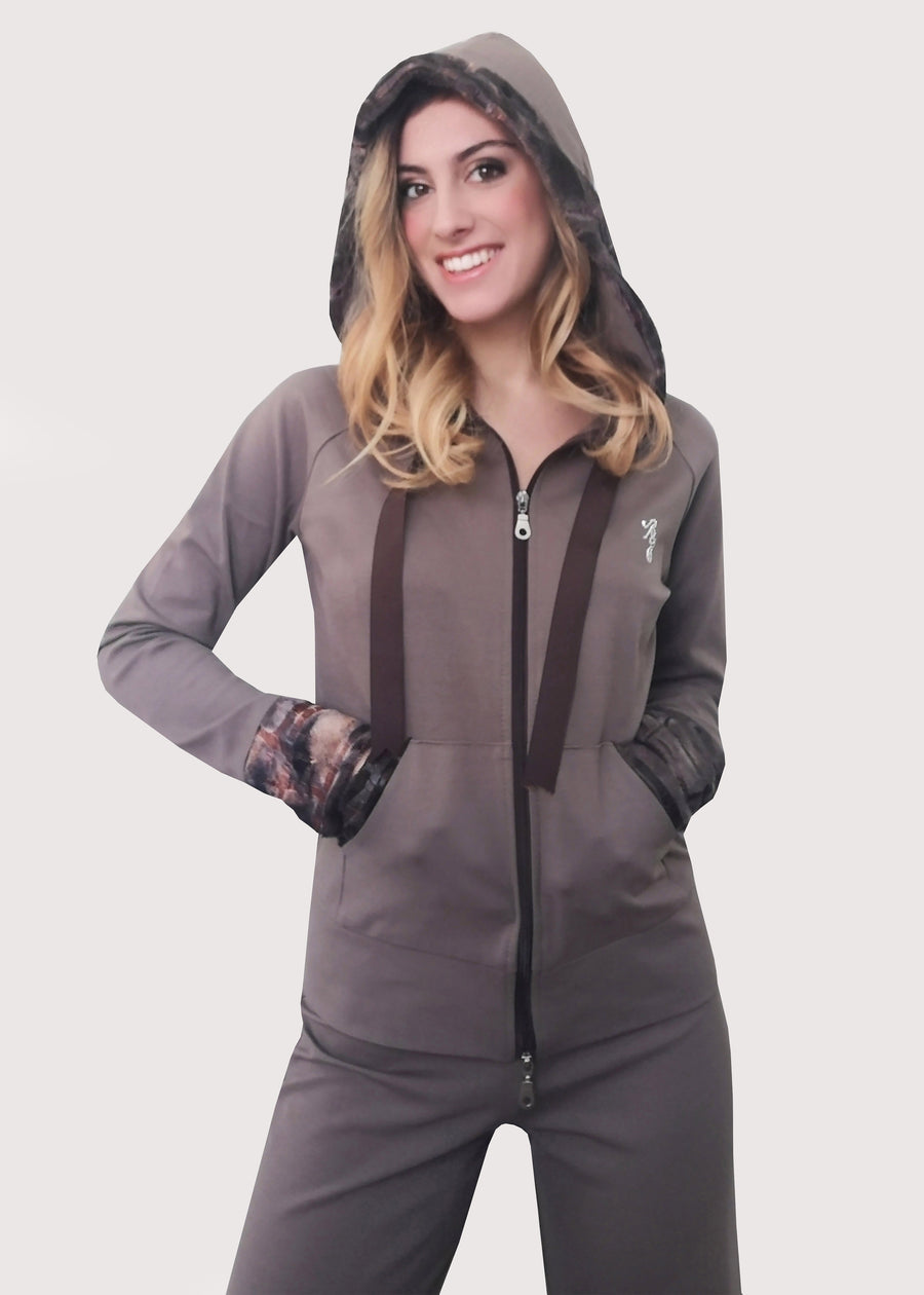Tuta sportiva elegante beige in calda viscosa stretch con cappuccio invernale. I bordi dei polsi e delle tasche sono in ecopelliccia. Un raffinato nastro in grogrè, è inserito nel bordo del cappuccio, per arricciarlo delicatamente. La tuta completo ha l'applicazione del logo Millyblu in strass. Il pantalone con elastico in vita è morbido e confortevole, dalla linea scivolata. 