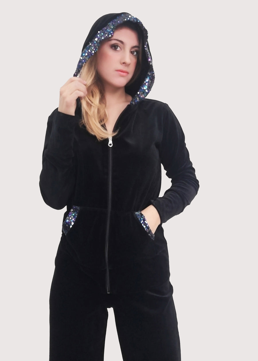Tuta Completo in ciniglia nera sporty chic. La felpa con cappuccio è rifinita internamente e ha gli inserti in paillettes sul cappuccio e sulle tasche. Il pantalone morbido ha un'ottima vestibilità, con l'elastico in vita e la coulisse nell'orlo, per poter regolare la lunghezza del pantalone come si preferisce.