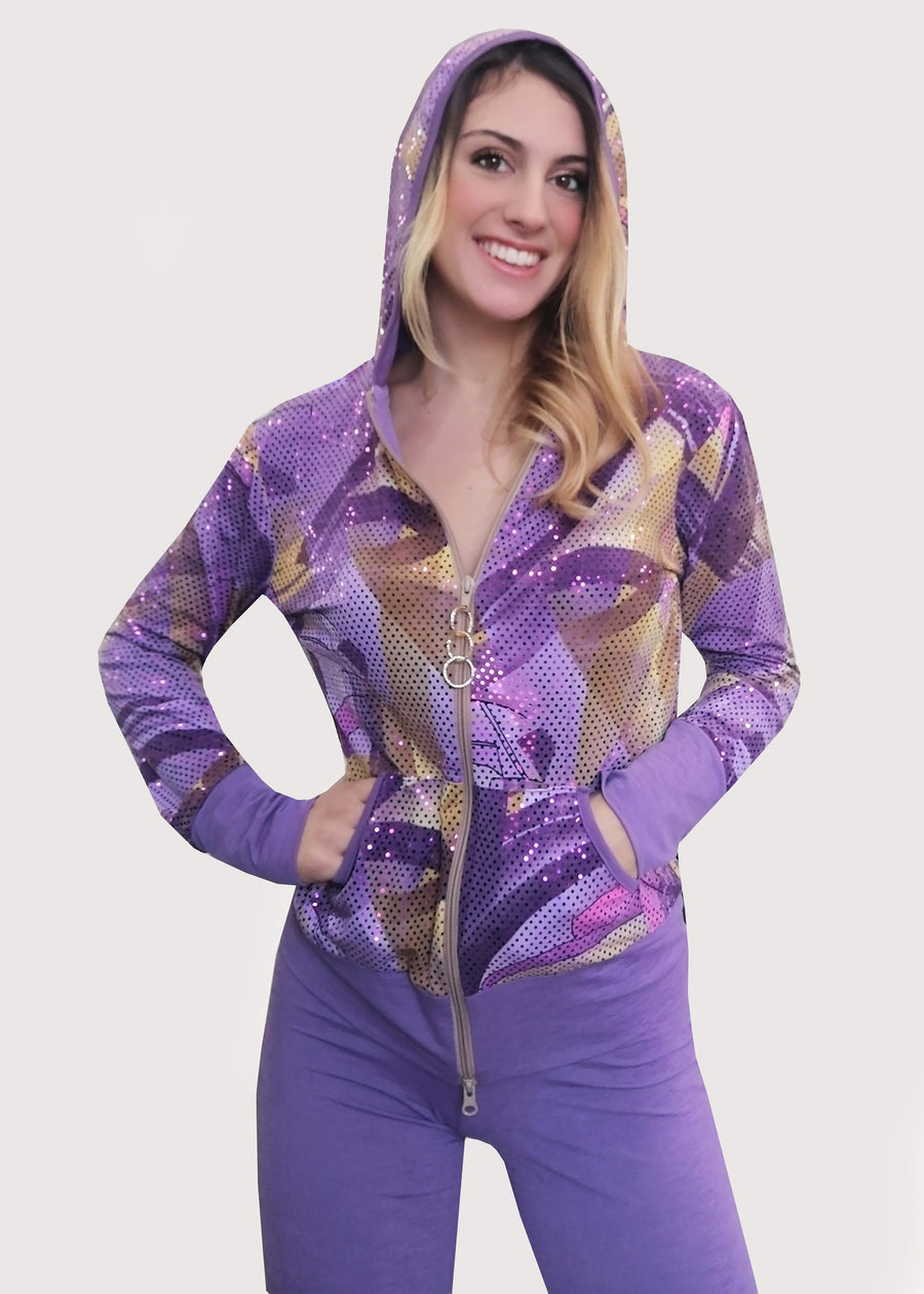 Tuta lilla in maglina e paillettes fantasia, con cinta, polsi e interno del cappuccio in maglina rivestita di stampa in paillettes. Il pantalone è semplice e scivola dritto, ampio alla caviglia, con elastico in vita.