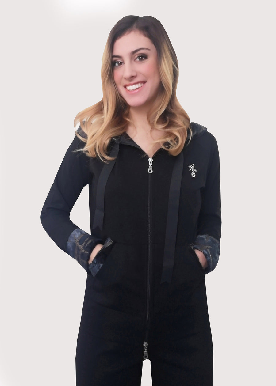 Tuta sportiva elegante nera in calda viscosa stretch con cappuccio invernale. I bordi dei polsi e delle tasche sono in ecopelliccia. Un raffinato nastro in grogrè, è inserito nel bordo del cappuccio, per arricciarlo delicatamente. La tuta completo ha l'applicazione del logo Millyblu in strass. Il pantalone con elastico in vita è morbido e confortevole, dalla linea scivolata. 