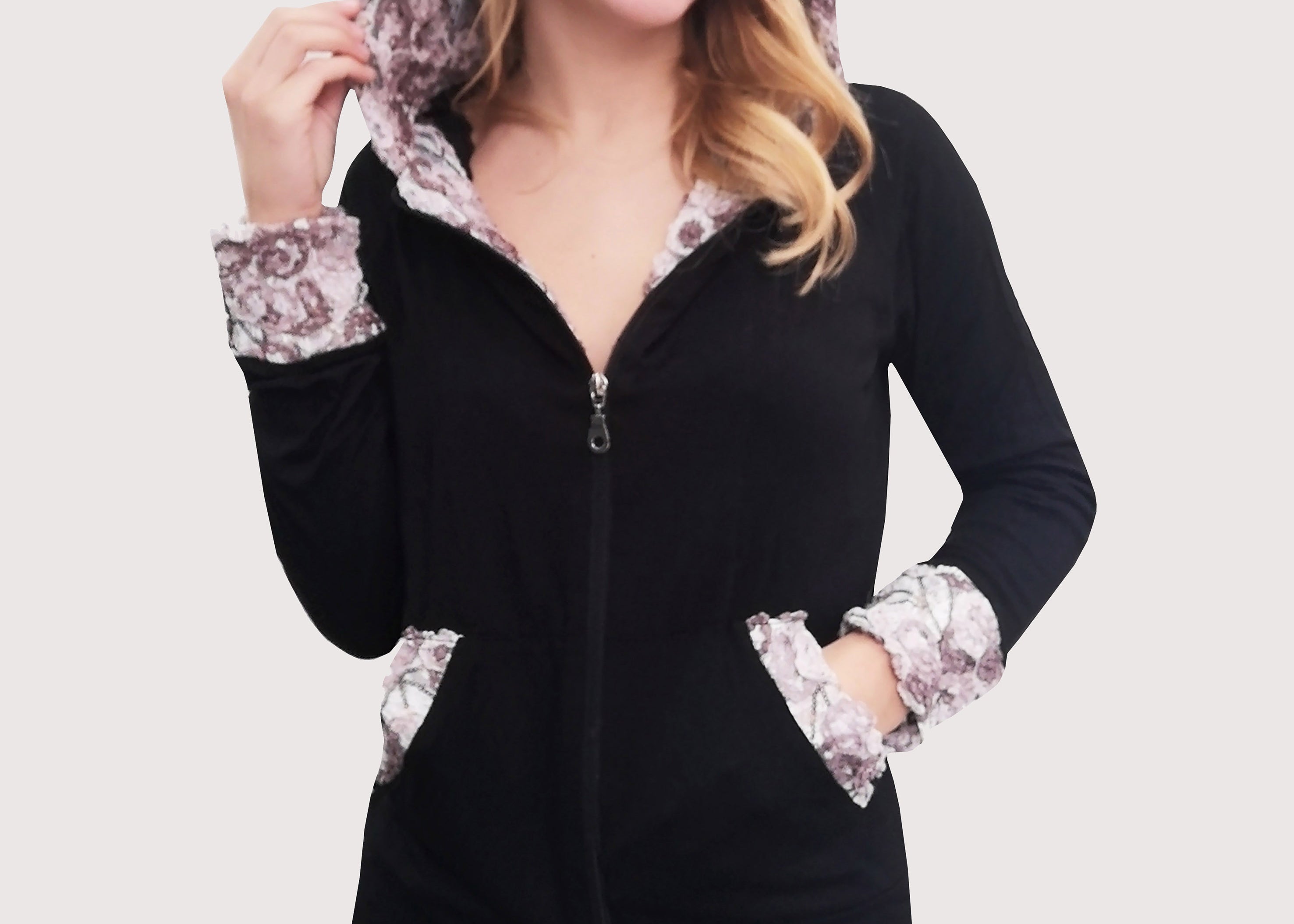 Tuta nera in viscosa con cappuccio, polsi e tasche in pizzo dai disegni in rilievo panna e beige. Outfit mezza stagione. Il pantalone, con la baschina doppia e l'elastico inserito in vita, ha una linea leggermente ampia.