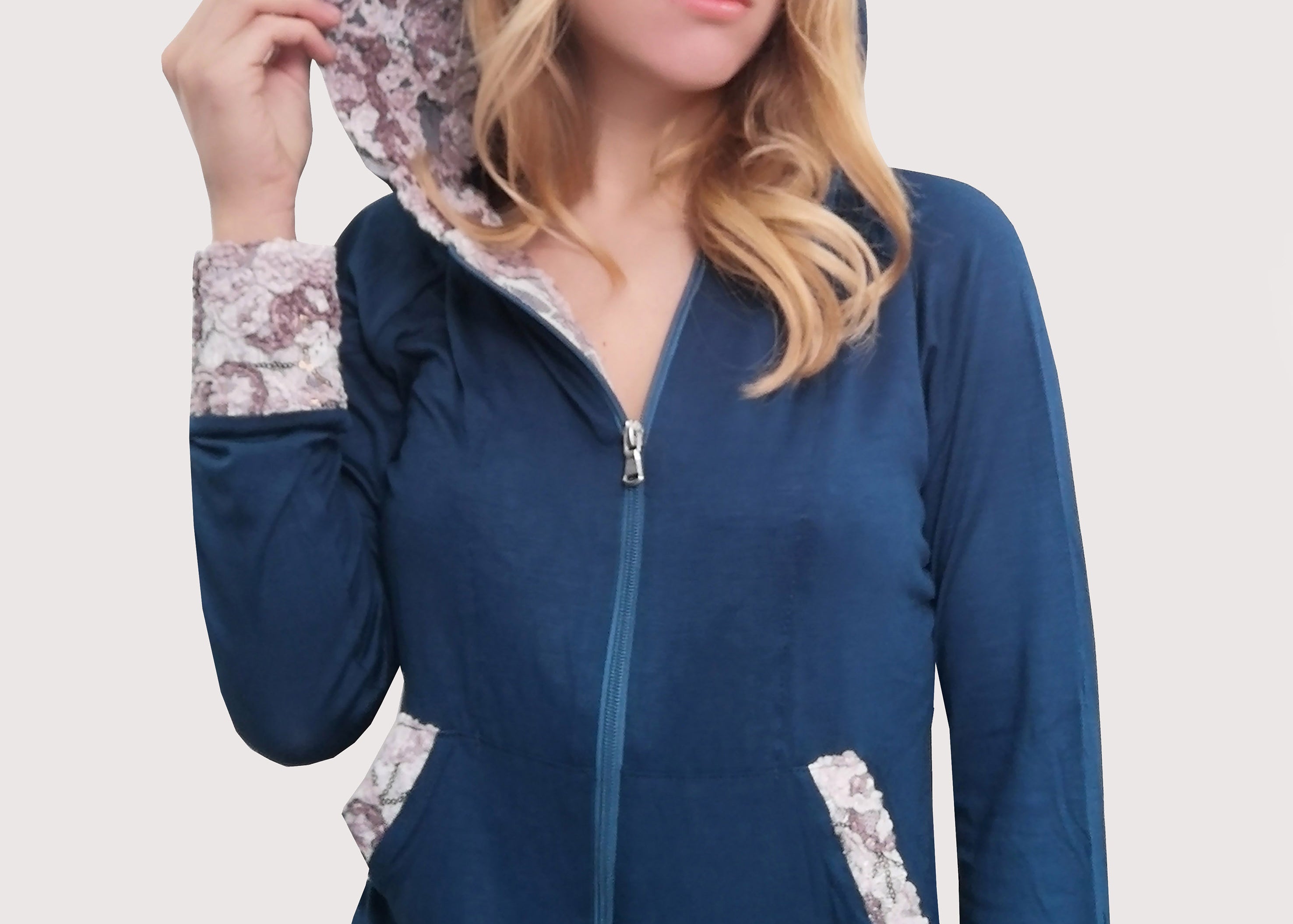 Tuta in viscosa elastica ottanio con cappuccio, polsi e tasche in pizzo dai disegni in rilievo panna e beige. Outfit mezza stagione. Il pantalone, con la baschina doppia e l'elastico inserito in vita, ha una linea leggermente ampia in fondo con la coulisse, che permette di regolare l'ampiezza e la lunghezza come meglio si desidera.