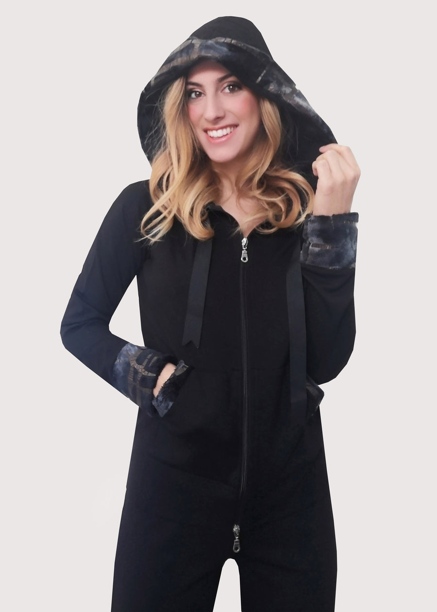 Tuta sportiva elegante nera in calda viscosa stretch con cappuccio invernale. I bordi dei polsi e delle tasche sono in ecopelliccia. Un raffinato nastro in grogrè, è inserito nel bordo del cappuccio, per arricciarlo delicatamente. La tuta completo ha l'applicazione del logo Millyblu in strass. Il pantalone con elastico in vita è morbido e confortevole, dalla linea scivolata. 
