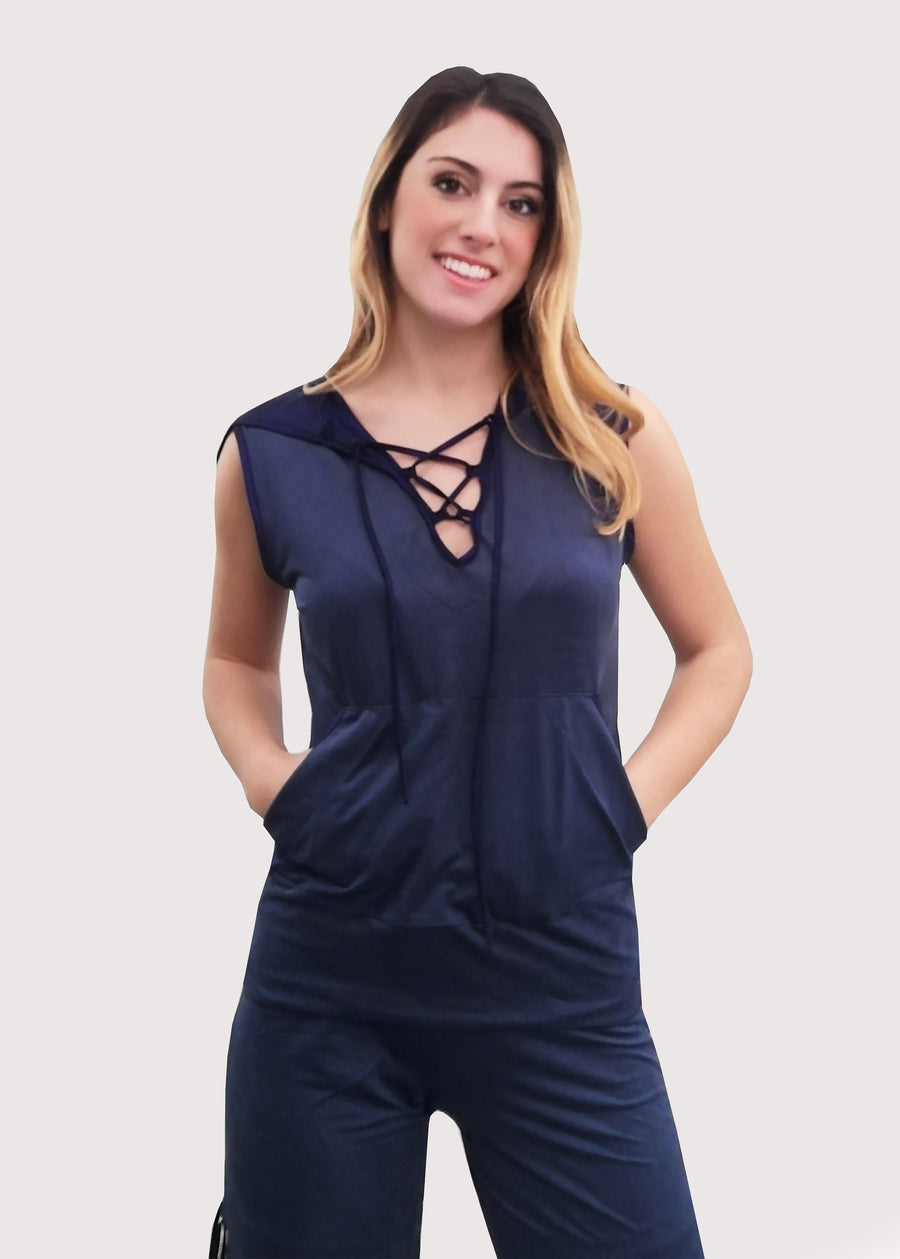 Tuta Completo in dainetto stretch con cappuccio foderato in jersey satinato. Scollo a V con lacci incrociati, senza maniche e tasche a marsupio. Il pantalone con elastico in vita, ha la coulisse sull'orlo per poterlo regolare come si desidera. Il budellino inserito sui lati del pantalone, crea un fiocco, donando movimento alla silhouette.