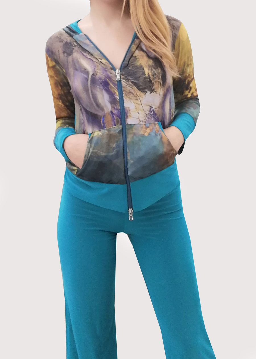 Tuta in maglina color smeraldo con cappuccio. Il giubbino riporta una delle nostre stampe, dal dipinto "Futura". Il pantalone è a tinta unita con la baschina doppiata e l'elastico in vita, dalla linea semplice e leggermente svasata in fondo. Particolare ed elegante nella sua essenza.
