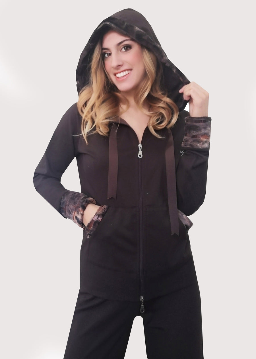 Tuta sportiva elegante marrone in calda viscosa stretch con cappuccio invernale. I bordi dei polsi e delle tasche sono in ecopelliccia. Un raffinato nastro in grogrè, è inserito nel bordo del cappuccio, per arricciarlo delicatamente. La tuta completo ha l'applicazione del logo Millyblu in strass. Il pantalone con elastico in vita è morbido e confortevole, dalla linea scivolata. 