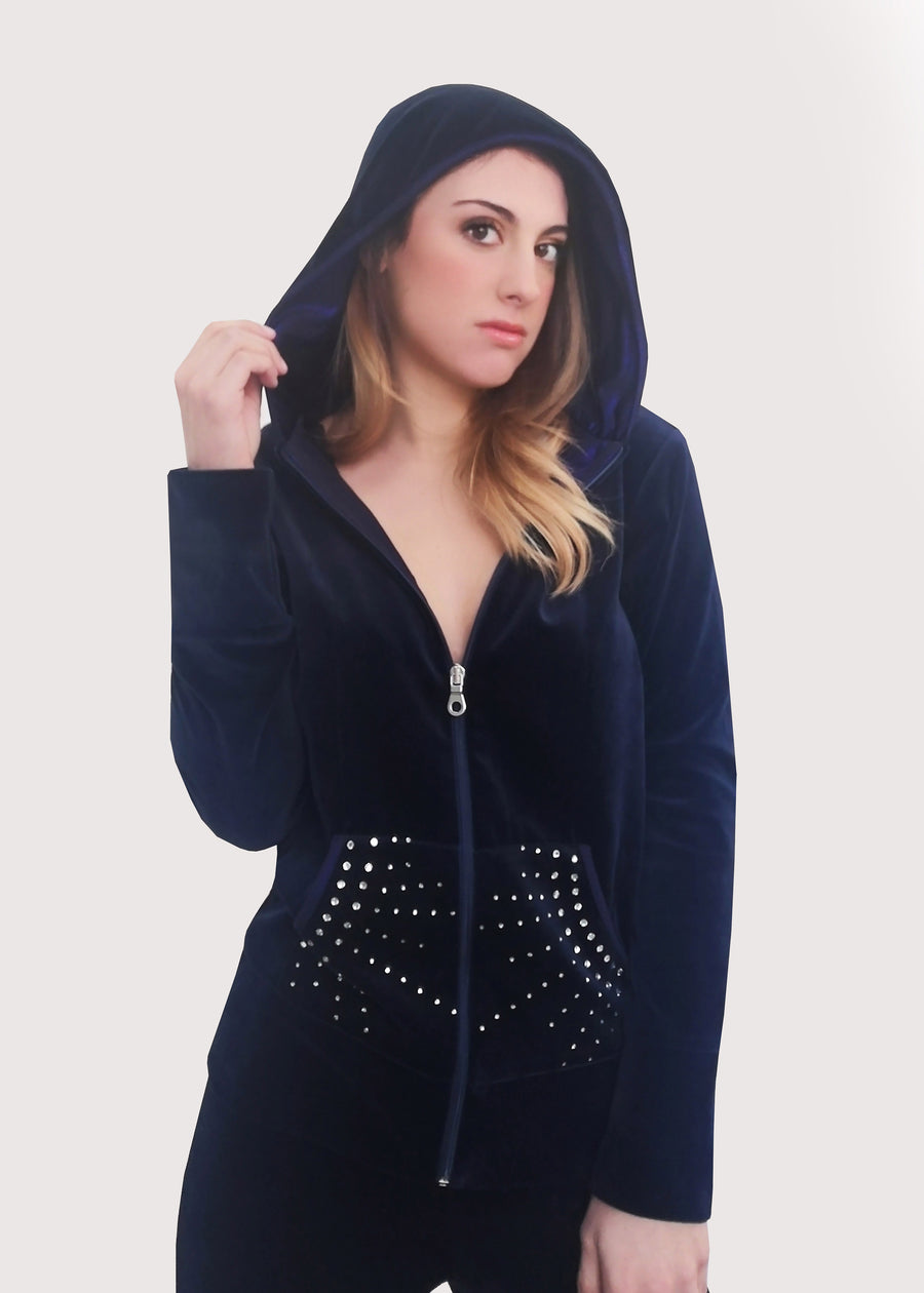 Tuta blu in ciniglia con strass sulle tasche. La felpa con cappuccio è doppiato in maglina satinata cangiante, con cerniera lampo. Il pantalone morbido ha l'elastico in vita e la coulisse nell'orlo.