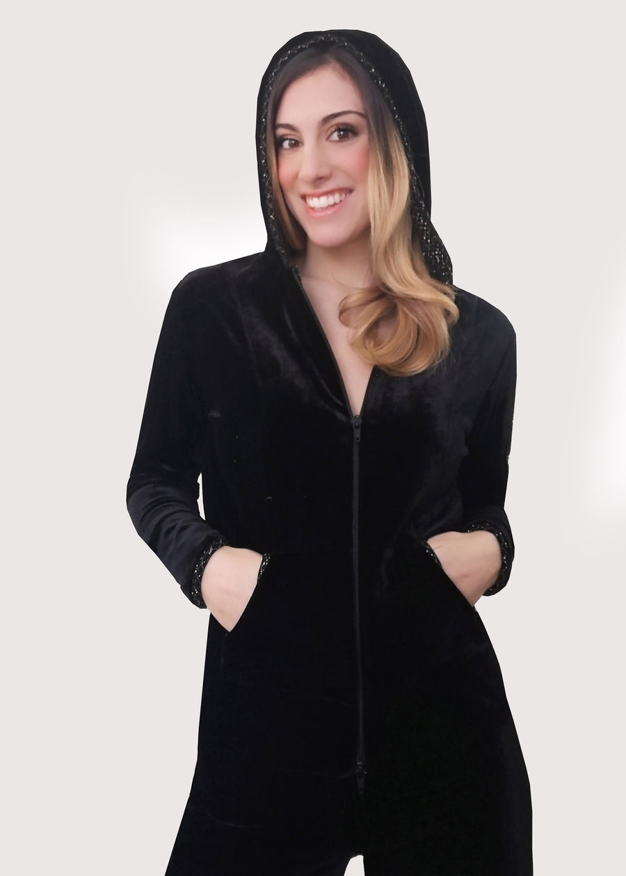Completo tuta elegante in velluto nero. La tuta con cappuccio ha la cerniera lampo e lo stemma ricamato sulla manica. Gli interni della tuta sono in maglina lurex oro. Il pantalone morbido in velluto nero ha l'elastico in vita e la coulisse regolabile inserita nell'orlo.