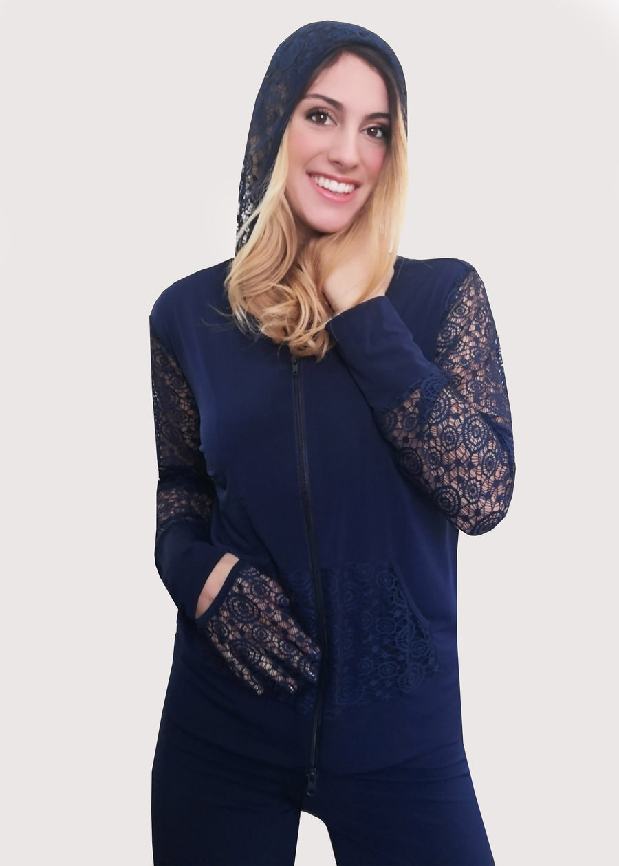 Tuta blu con inserti in pizzo e cappuccio in maglina elastica. La felpa, il cappuccio e le tasche sono in pizzo, nello stesso colore abbinato e con la zip sul davanti. Il pantalone ha l'elastico e la doppia baschina in vita con un'ottima vestibilità che dona sinuosità alle forme femminili. Leggermente ampio all'orlo.