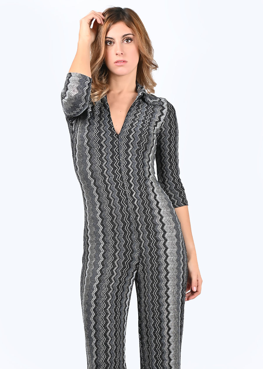 Tuta intera elegante Elena in lurex geometrico argento. La profondità della scollatura è regolabile, grazie alla zip invisibile che permette di indossare il capo sia con il collo alto sia con scollo a V. La manica della tuta è a 3/4. Il modello è a vita alta con pantalone dalla linea scivolata.